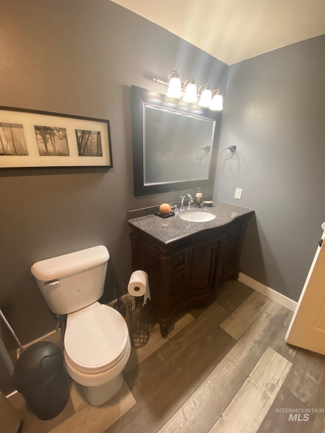 half bath featuring toilet, baseboards, vanity, and wood finished floors