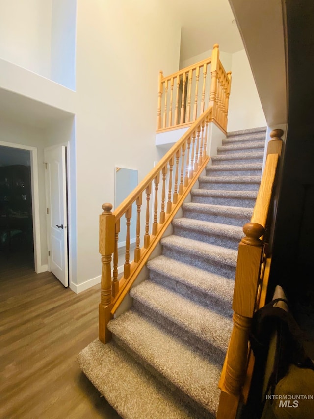 staircase with baseboards, a towering ceiling, and wood finished floors