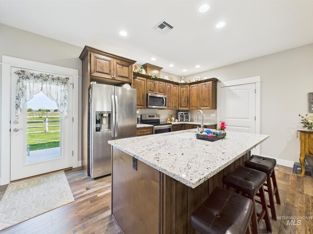 kitchen featuring appliances with stainless steel finishes, light stone counters, recessed lighting, a kitchen island with sink, and dark wood-style flooring