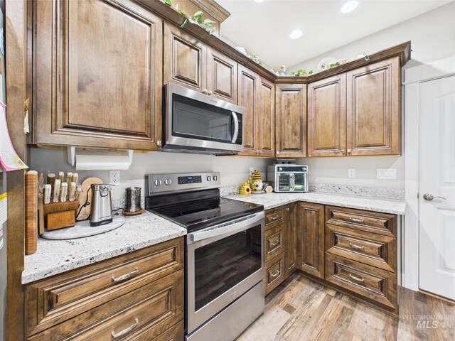 kitchen with stainless steel appliances, light wood-style flooring, light stone countertops, and recessed lighting