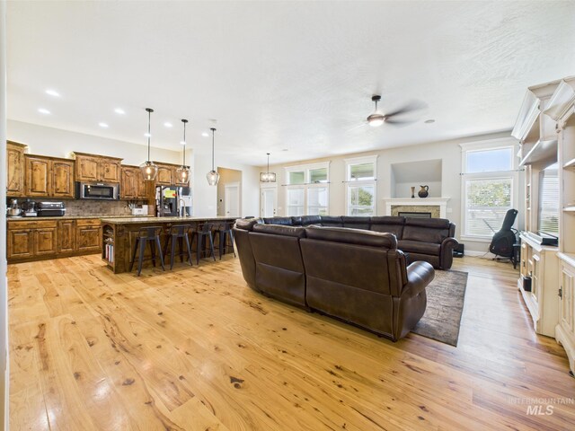 living area with a ceiling fan, light wood-style flooring, a fireplace, and recessed lighting