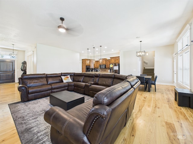 living room with stairway, a chandelier, light wood-type flooring, a ceiling fan, and baseboards