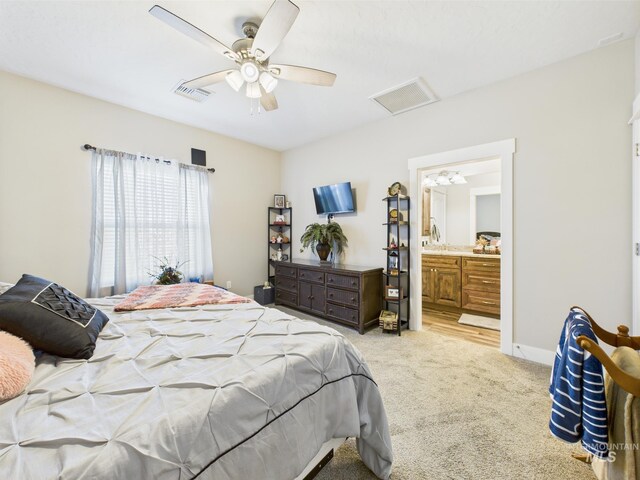 bedroom featuring light carpet, ensuite bathroom, and a ceiling fan