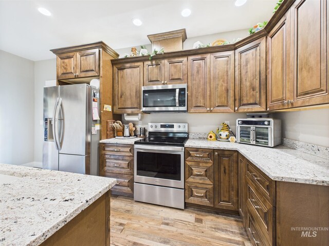 kitchen with stainless steel appliances, light wood-style flooring, light stone counters, and recessed lighting