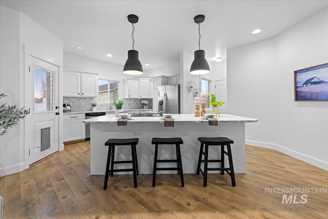 kitchen with appliances with stainless steel finishes, light wood-type flooring, pendant lighting, white cabinets, and a breakfast bar area