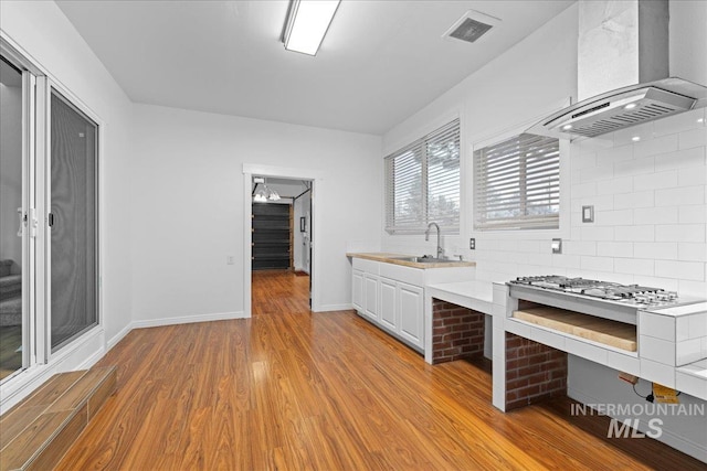 kitchen featuring white cabinetry, sink, wall chimney range hood, tasteful backsplash, and light wood-type flooring