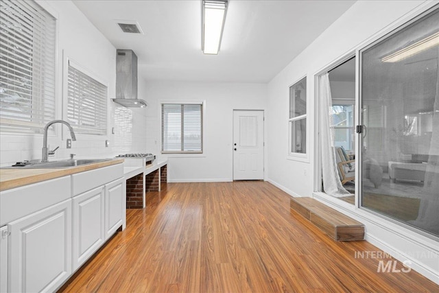 kitchen featuring white cabinets, plenty of natural light, wall chimney range hood, and sink