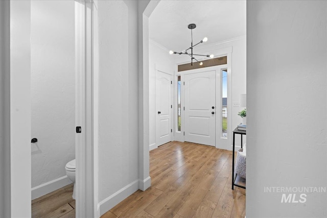 foyer featuring light wood-type flooring, crown molding, and a notable chandelier