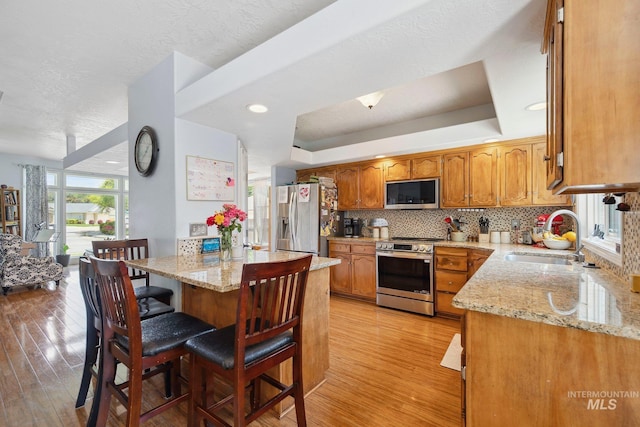 1229 N Hiltonhead Way, Eagle, ID 83616 - kitchen featuring appliances with stainless steel finishes, a sink, light wood-type flooring, light stone countertops, and a textured ceiling