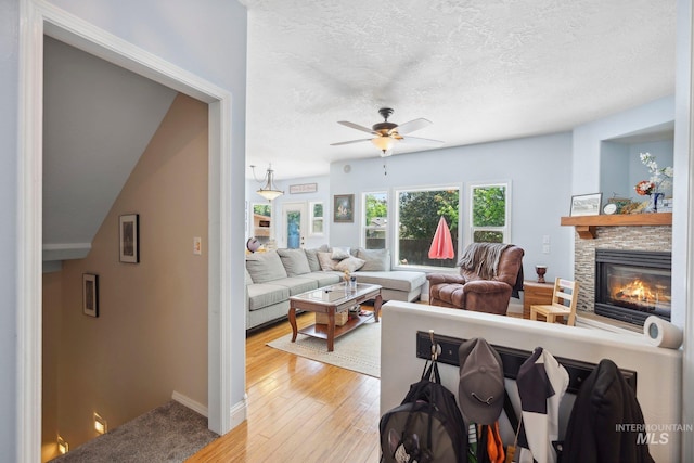 1229 N Hiltonhead Way, Eagle, ID 83616 - living area with a textured ceiling, a ceiling fan, a fireplace, light wood-style floors, and baseboards