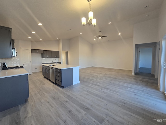 kitchen featuring light hardwood / wood-style flooring, appliances with stainless steel finishes, hanging light fixtures, backsplash, and a center island with sink