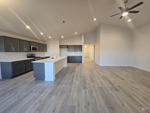 kitchen with sink, appliances with stainless steel finishes, backsplash, light hardwood / wood-style floors, and an island with sink