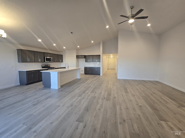 kitchen with sink, backsplash, a kitchen island with sink, stainless steel appliances, and light hardwood / wood-style flooring