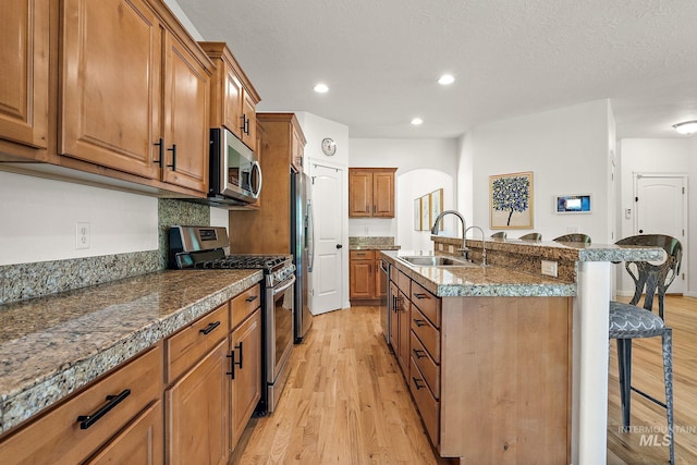 4902 N Schubert Ave, Meridian, ID 83646 - kitchen featuring stainless steel appliances, a breakfast bar, brown cabinets, a sink, and arched walkways