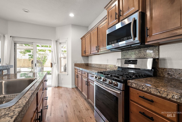 4902 N Schubert Ave, Meridian, ID 83646 - kitchen featuring stainless steel appliances, dark countertops, light wood-style floors, brown cabinetry, and recessed lighting
