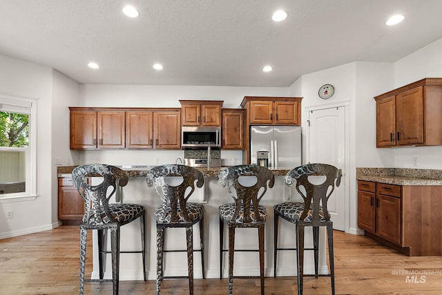 4902 N Schubert Ave, Meridian, ID 83646 - kitchen featuring appliances with stainless steel finishes, brown cabinetry, a kitchen bar, baseboards, and light wood finished floors