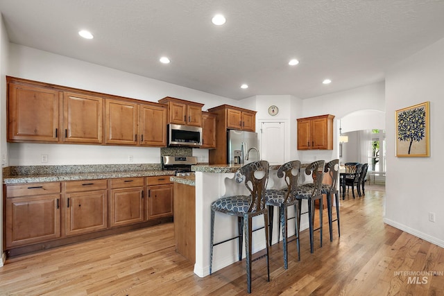 4902 N Schubert Ave, Meridian, ID 83646 - kitchen featuring stainless steel appliances, arched walkways, brown cabinetry, a breakfast bar, and a center island with sink