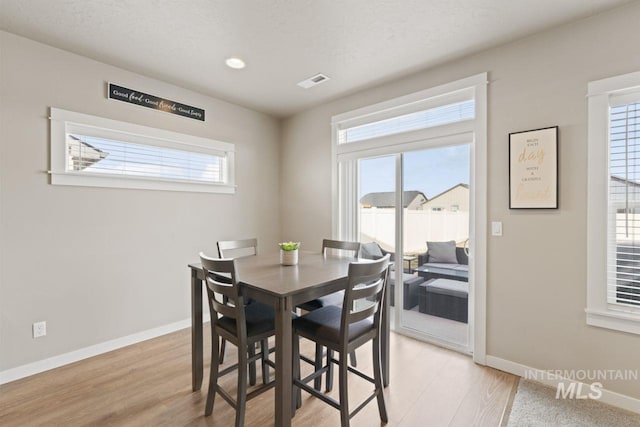 dining area with a textured ceiling, visible vents, baseboards, and light wood-type flooring