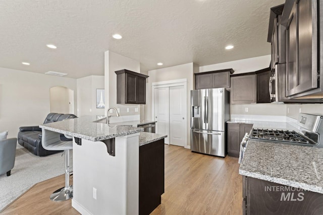 kitchen featuring dark brown cabinetry, arched walkways, open floor plan, and stainless steel appliances