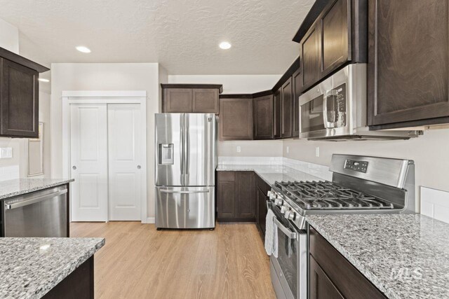 kitchen with dark brown cabinets, stainless steel appliances, light wood-style flooring, and light stone countertops