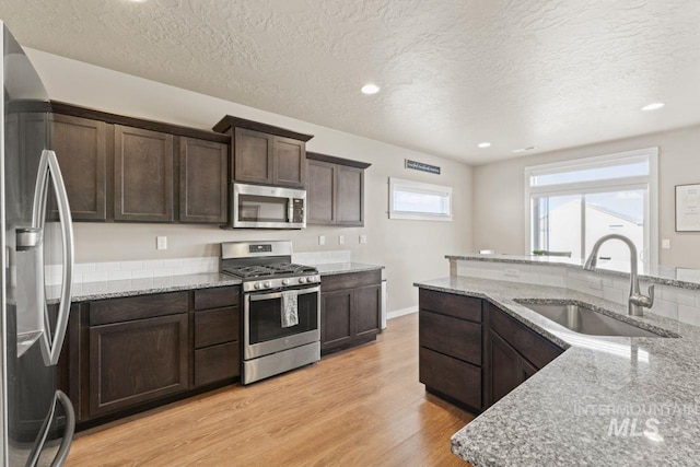 kitchen featuring light wood finished floors, dark brown cabinetry, light stone counters, appliances with stainless steel finishes, and a sink