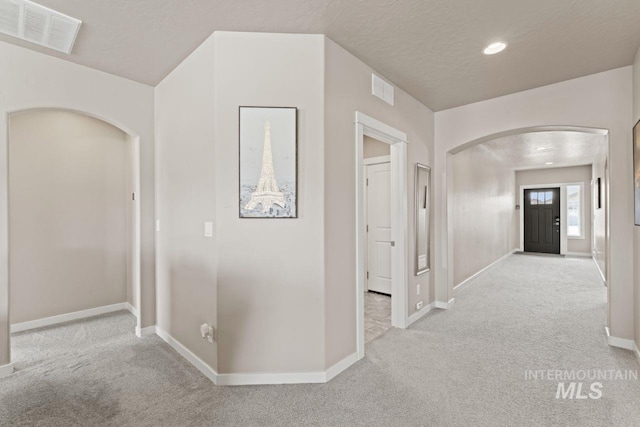 corridor with visible vents, arched walkways, carpet floors, and a textured ceiling