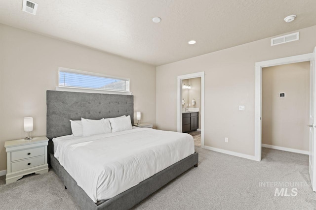 bedroom featuring visible vents, baseboards, light colored carpet, and ensuite bathroom