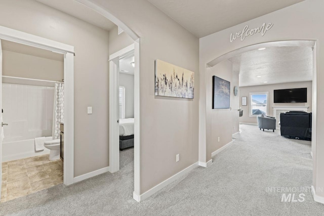 hallway with arched walkways, carpet flooring, and baseboards