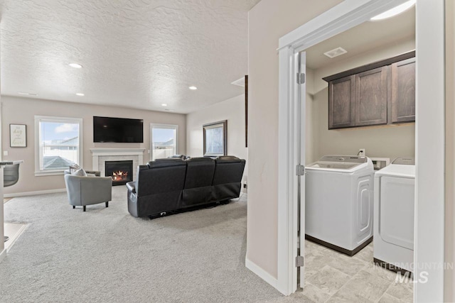 living area with baseboards, washing machine and dryer, light carpet, a warm lit fireplace, and a textured ceiling