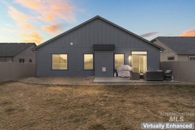 back of property at dusk featuring a yard, a patio area, board and batten siding, and a fenced backyard