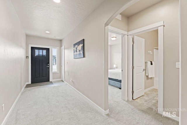 entrance foyer with baseboards, arched walkways, a textured ceiling, and carpet flooring