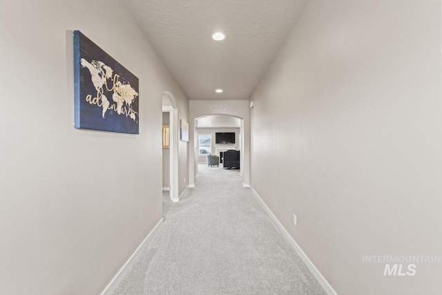 hallway with baseboards, carpet, recessed lighting, arched walkways, and a textured ceiling