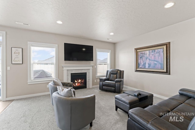 carpeted living room with visible vents, baseboards, recessed lighting, a lit fireplace, and a textured ceiling
