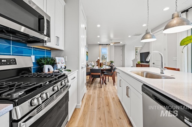 kitchen featuring light wood-type flooring, a sink, tasteful backsplash, appliances with stainless steel finishes, and white cabinets