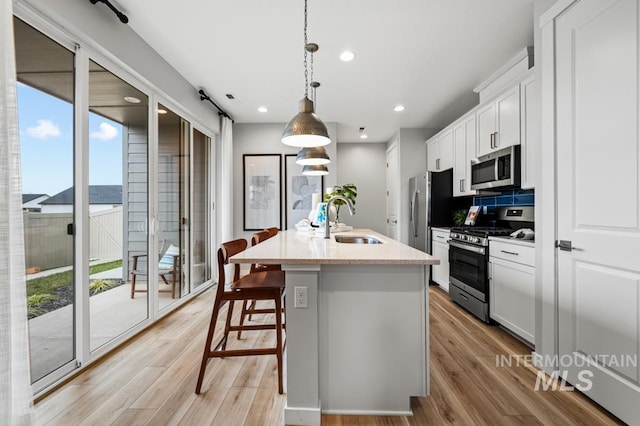 kitchen with a breakfast bar, an island with sink, a sink, appliances with stainless steel finishes, and light wood finished floors