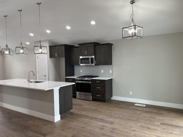 kitchen with sink, a center island with sink, appliances with stainless steel finishes, pendant lighting, and decorative backsplash