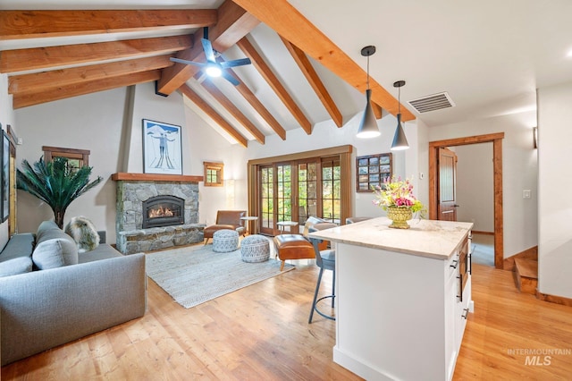 living room featuring ceiling fan, a stone fireplace, beamed ceiling, high vaulted ceiling, and light wood-type flooring