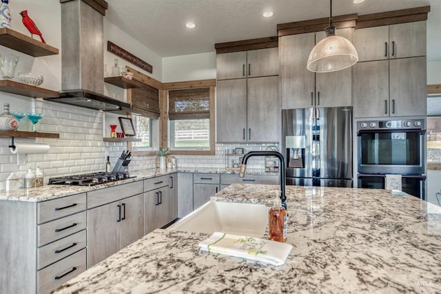kitchen featuring open shelves, light stone counters, island exhaust hood, a sink, and appliances with stainless steel finishes