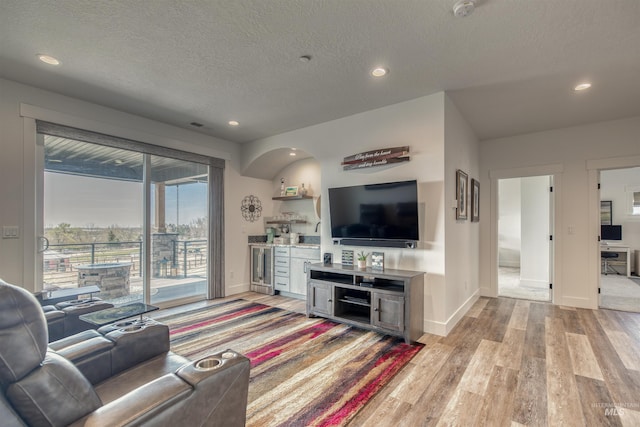 living room featuring a textured ceiling, a dry bar, baseboards, light wood-style floors, and recessed lighting