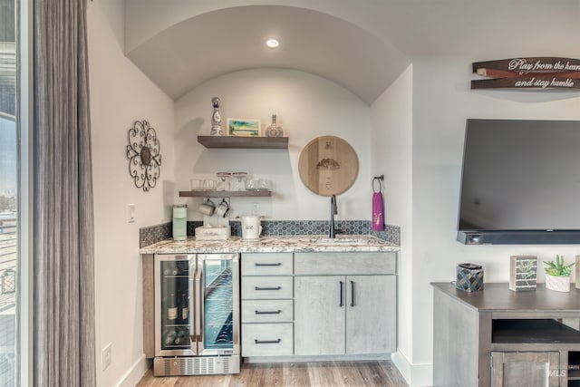 bar with wine cooler, baseboards, indoor wet bar, and light wood-style flooring