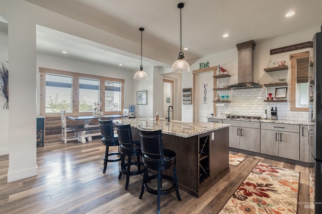 kitchen featuring wall chimney range hood, open shelves, recessed lighting, stainless steel gas stovetop, and wood finished floors