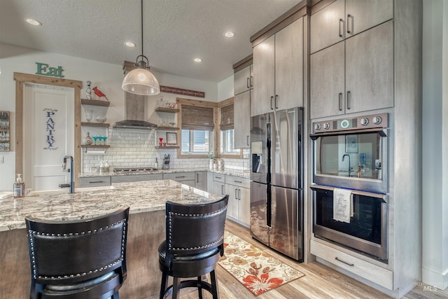 kitchen with a kitchen breakfast bar, appliances with stainless steel finishes, open shelves, light stone countertops, and light wood finished floors