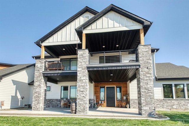 rear view of property with board and batten siding, a shingled roof, a balcony, and stone siding