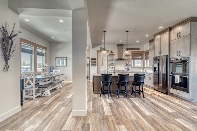 kitchen with light wood finished floors, double oven, wall chimney exhaust hood, baseboards, and black fridge with ice dispenser