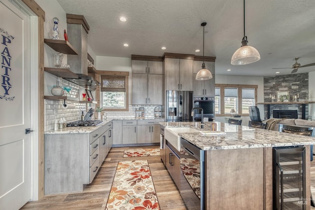 kitchen with a textured ceiling, appliances with stainless steel finishes, a sink, light wood finished floors, and wine cooler