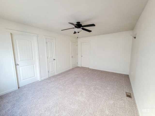 unfurnished bedroom with carpet floors, two closets, visible vents, a ceiling fan, and baseboards