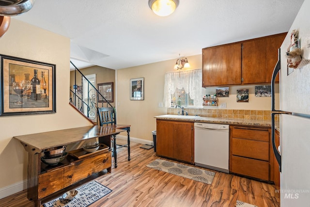 kitchen featuring white appliances, sink, pendant lighting, light hardwood / wood-style flooring, and a notable chandelier