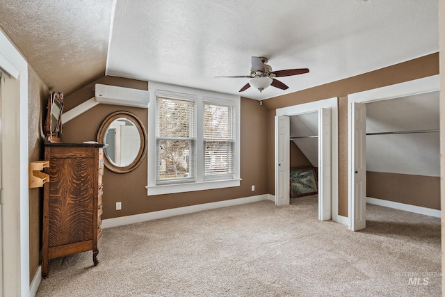 unfurnished bedroom with two closets, an AC wall unit, vaulted ceiling, ceiling fan, and a textured ceiling