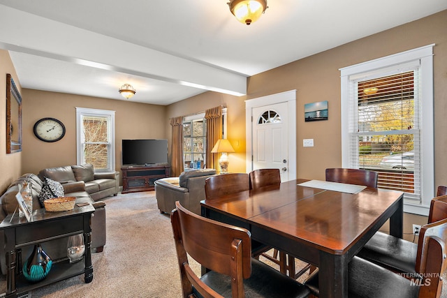 carpeted dining space with beamed ceiling