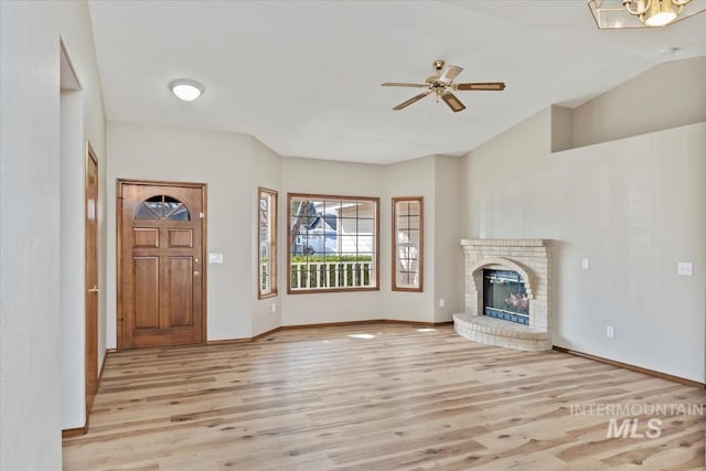 unfurnished living room with lofted ceiling, ceiling fan, a fireplace, baseboards, and light wood finished floors